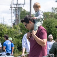 Man holds baby on shoulders as he looks at boats